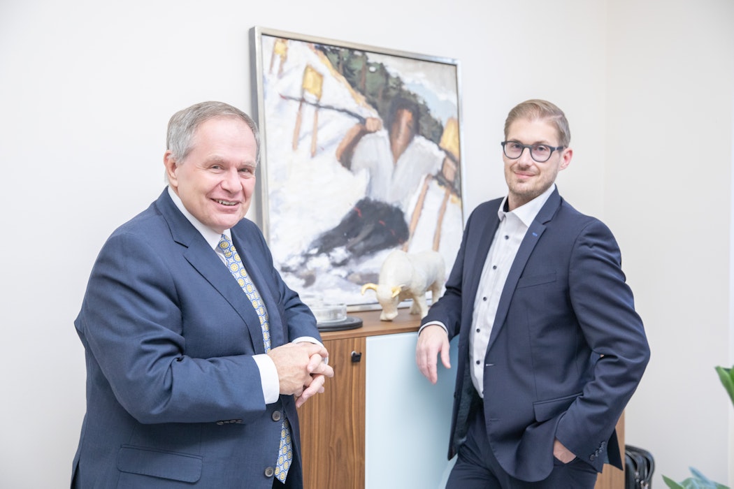 In einem hellen Raum hängt an der Wand ein Bild, daneben stehen die Gründer der Golden Gates AG Herbert Behr (Senior) und Constantin Behr (Junior).